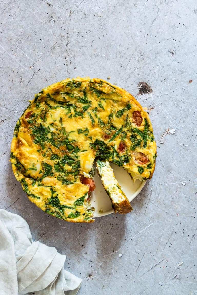 Top down view of the finished Smoked Haddock and Spinach Frittata with one slice removed and placed next to a white cloth napkin