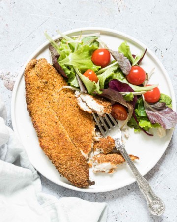 crispy air fryer fish fillet on a plate with some salad and a fork