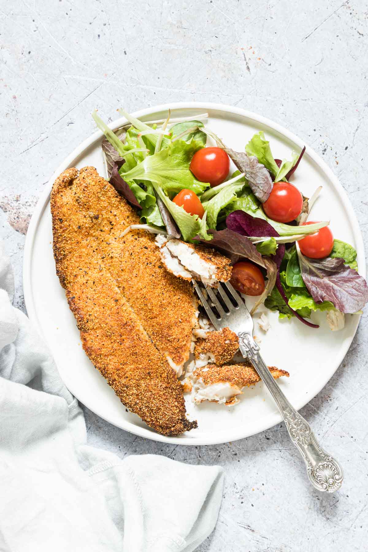 crispy air fryer fish fillet on a plate with some salad and a fork