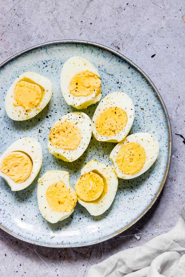 completed air fryer hard boiled eggs cut in half, seasoned with pepper and served on a blue ceramic plate