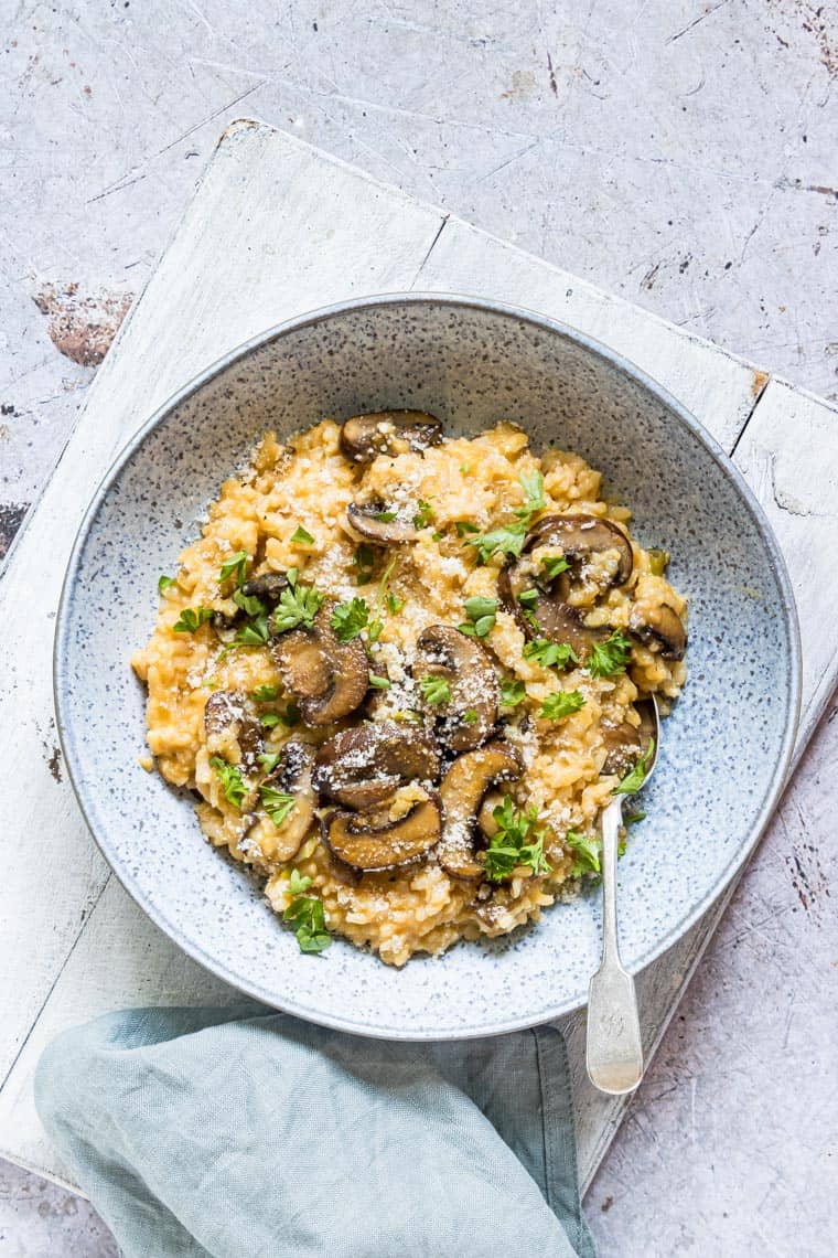 mushroom risotto served in a ceramic bowl with a spoon and blue cloth napkin
