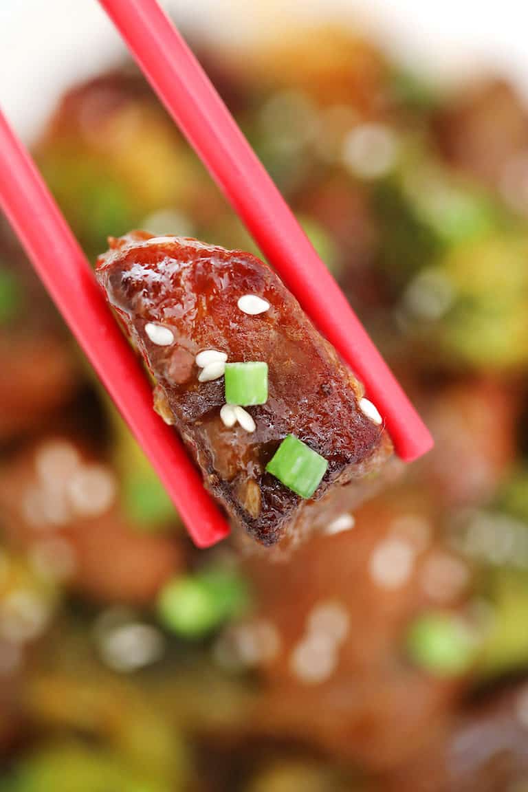 red chopsticks holding one piece if Instant Pot Beef and Broccoli garnished with green onions and sesame seeds