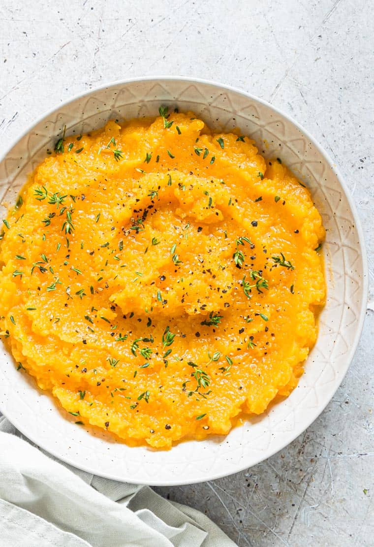 crockpot mashed butternut squash served in a white bowl and topped with herbs