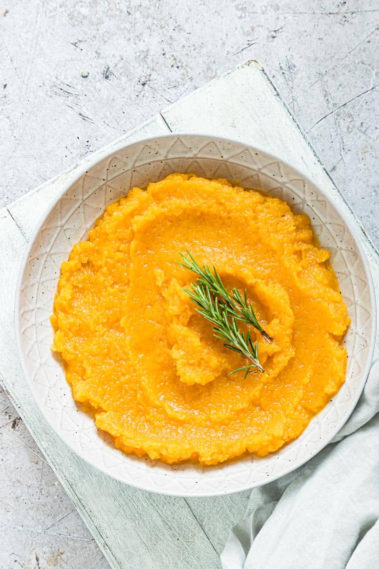 instant pot butternut squash mash in a white bowl and topped with fresh herbs