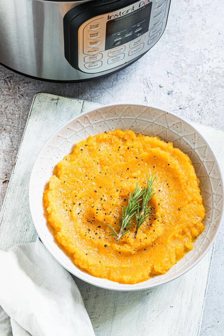 Instant Pot Mashed Butternut Squash in a ceramic bowl set in front of the Instant Pot