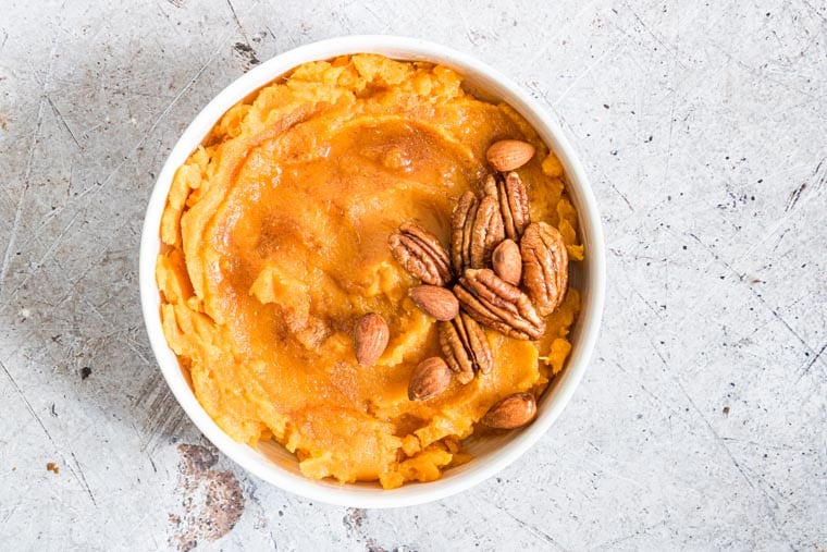 slow cooker mashed sweet potatoes in a white bowl and topped with pecans and almonds