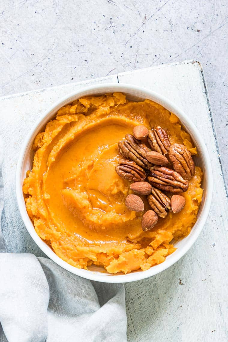 slow cooker mashed sweet potatoes topped with nuts and served in a white bowl