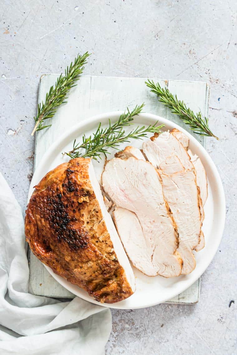 top down view of air fryer boneless turkey breast on a white plate surrounded with rosemary springs