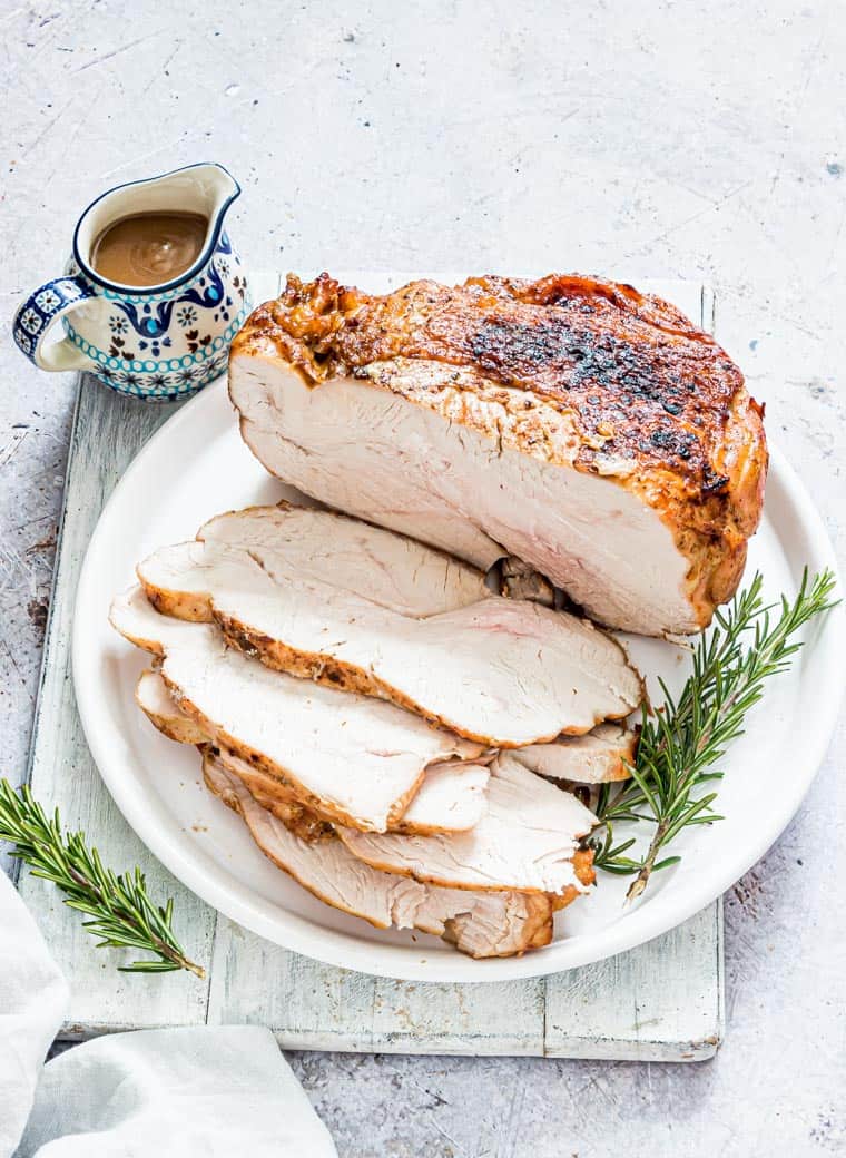 close up view of cooked turkey breast on a white platter with pitcher of gravy to the side.