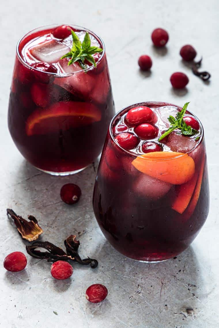 two glasses of hibiscus punch placed next to cranberries and dried hibiscus