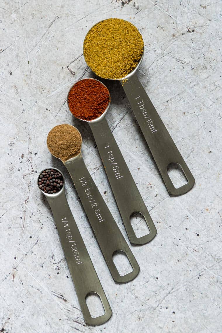 four measuring spoons filled with various spices