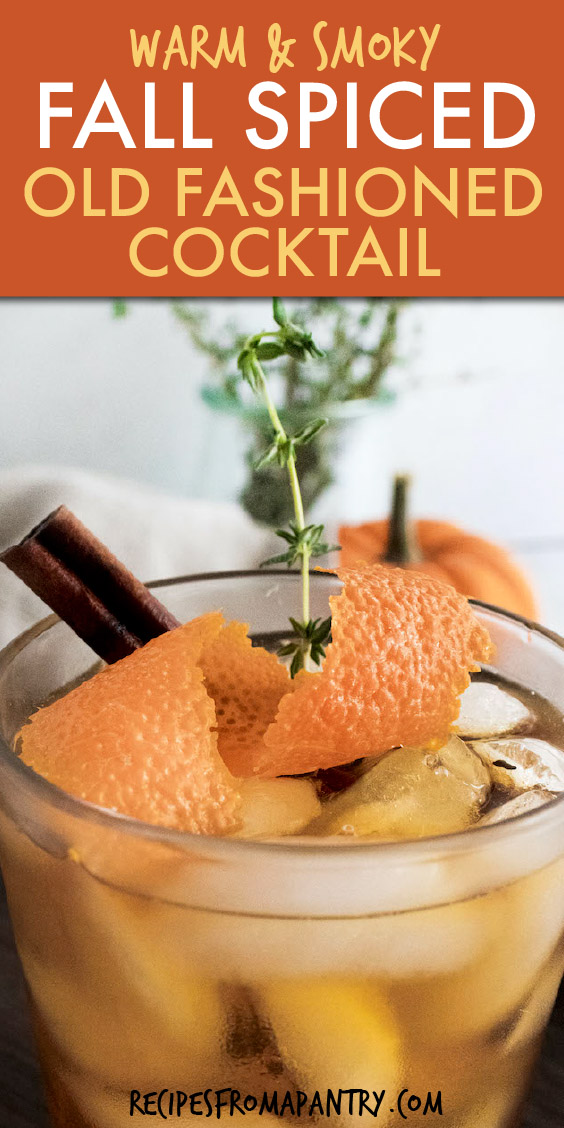 close up of a glass of iced cocktail garnished with orange peel and a sprig of thyme