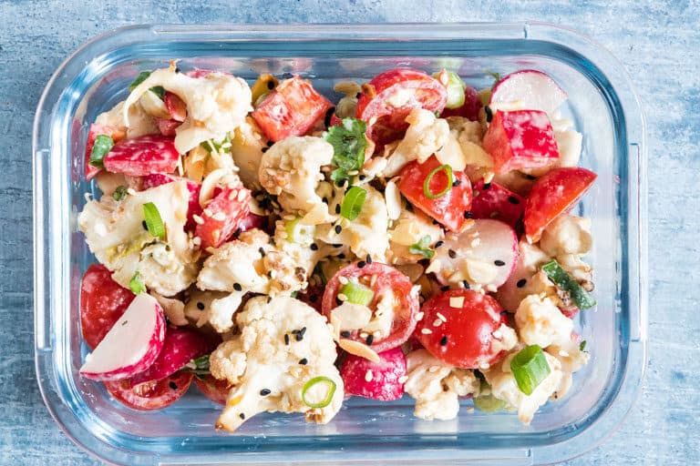 horizontal image of one glass meal prep container filled with cauliflower salad recipe.