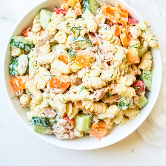 A creamy tuna pasta salad with green peas and red onions in a white bowl.