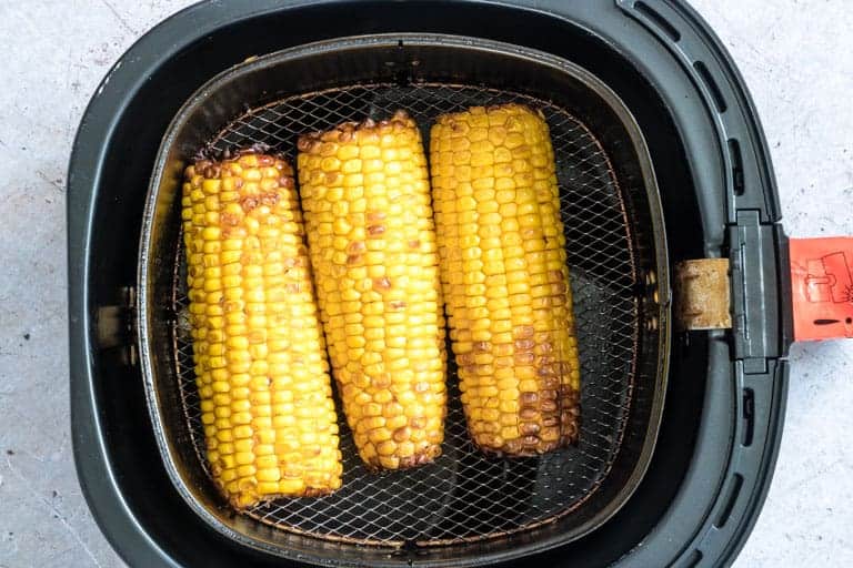 three pieces of cooked Air Fryer Corn on the Cob inside the air fryer basket