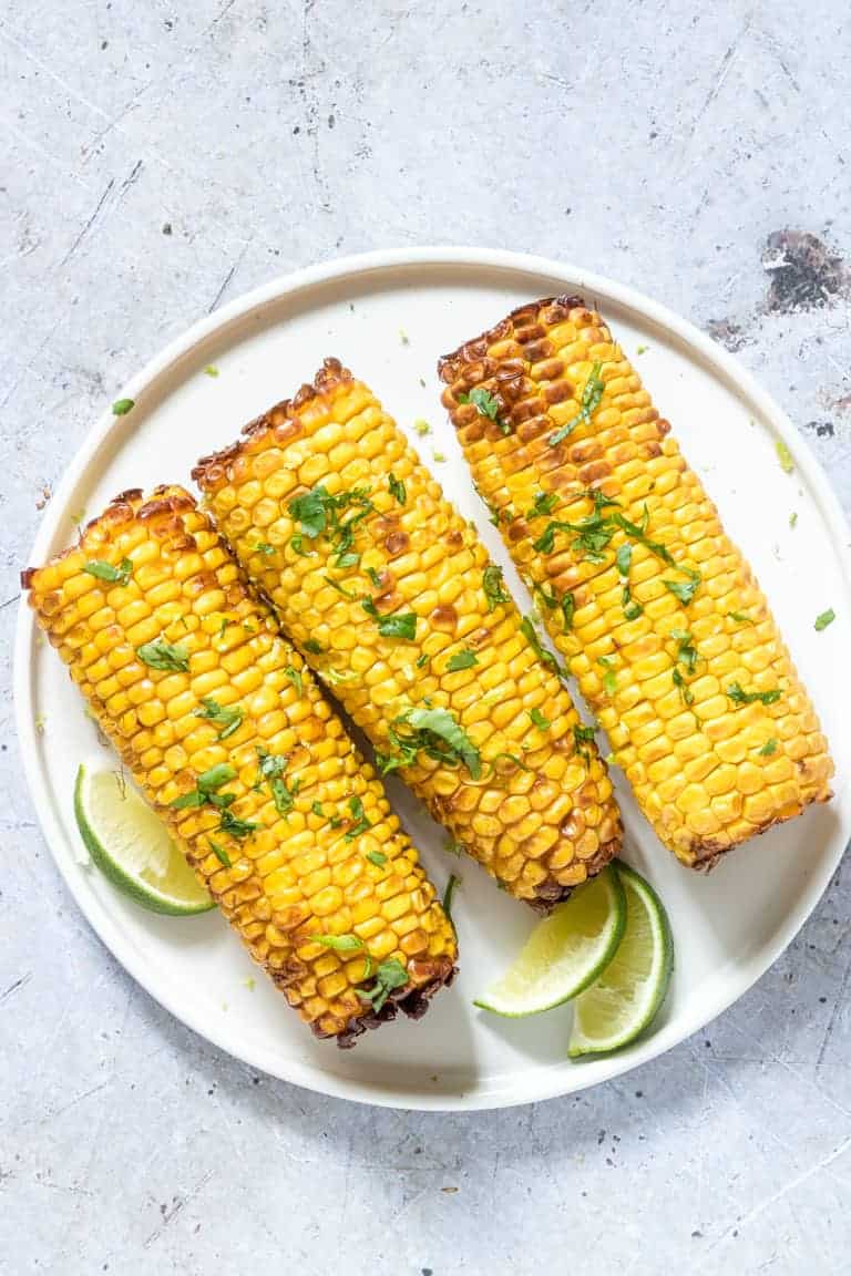 three pieces of Air Fryer Corn on the Cob topped with chopped fresh herbs and served with lime wedges