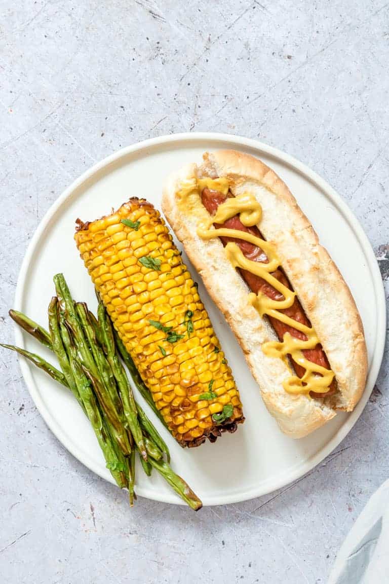 one air fryer hot dog served with an ear of air fryer corn on the cob and a portion of air fryer green beans