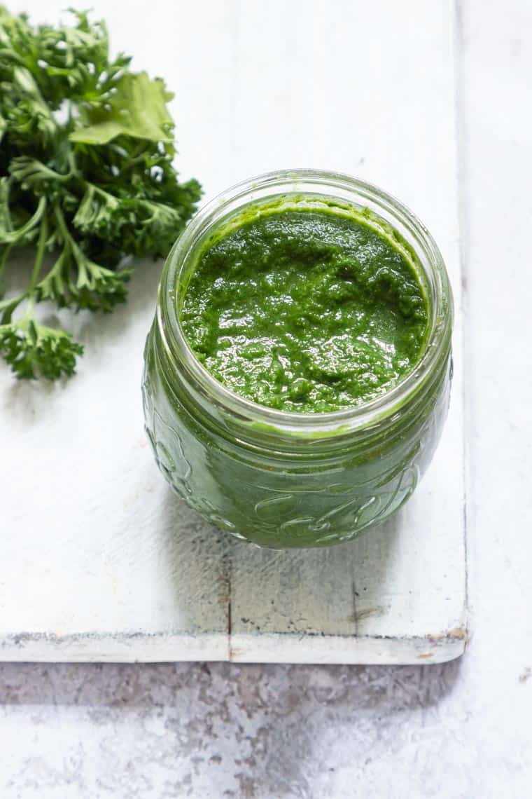 a jar of green seasoning next to a bunch of fresh parsley