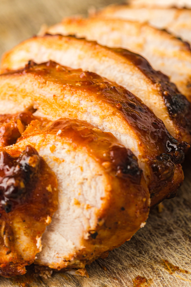 Sliced smoked chicken breast with barbecue glaze on a wooden board.