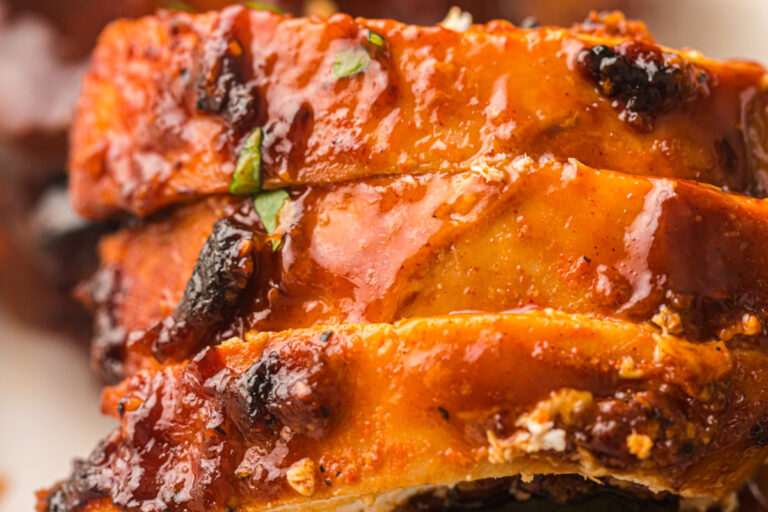 Close-up of sliced smoked chicken breast topped with barbecue glaze and herbs.