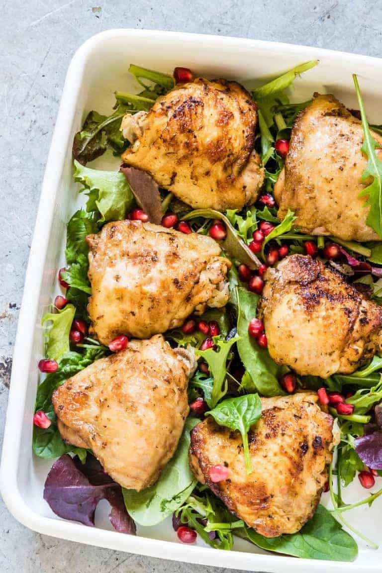 instant pot chicken thighs on a salad plate with salad leaves and pomegranate seeds