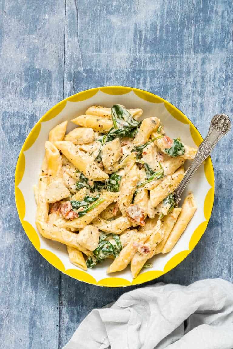 Instant Pot Creamy Tuscan Chicken Pasta served in a white bowl with yellow trim and a large silver spoon