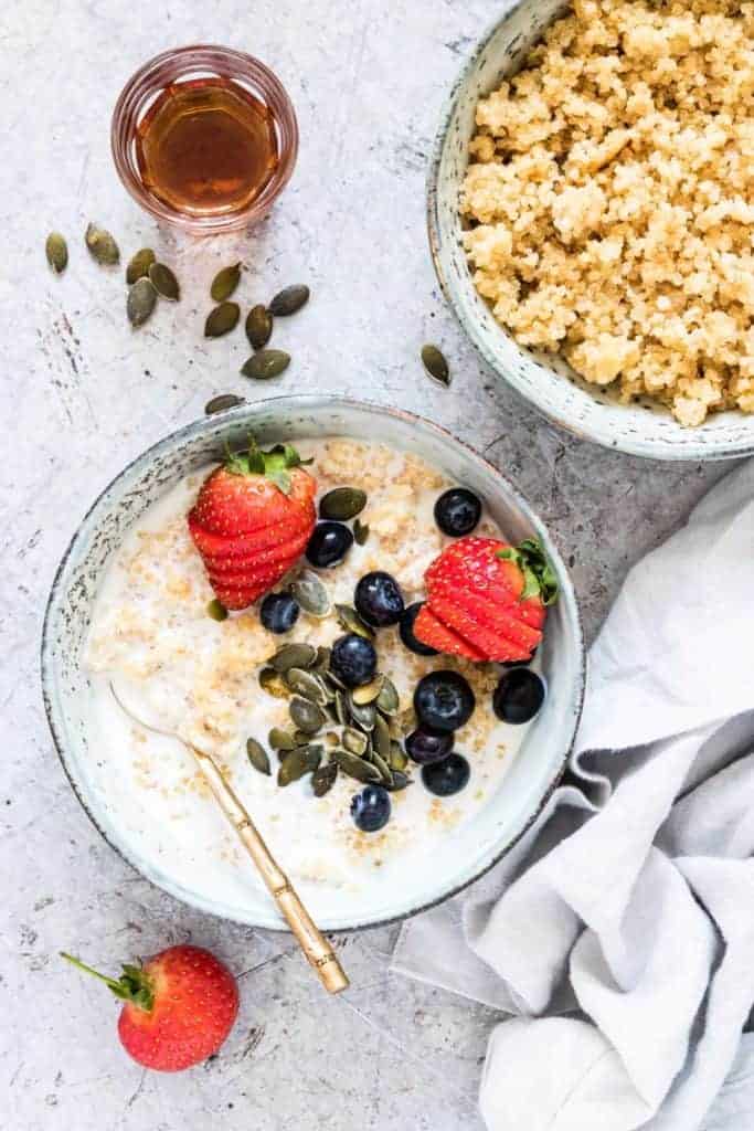 quinoa porridge served with berries and seeds in a blue bowl with gold spoon