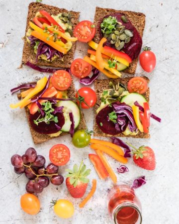 open-faced rainbow sandwich with colourful vegetables on top and around rainbow sandwiches