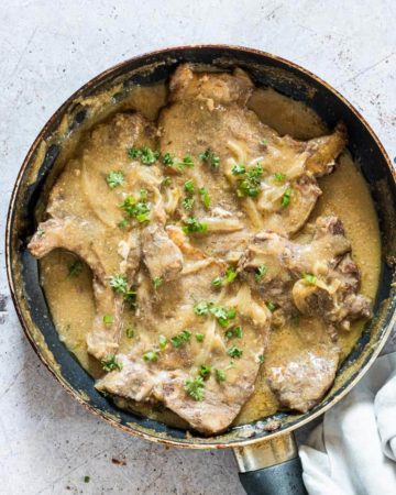 smothered pork chops in a pan and ready to serve