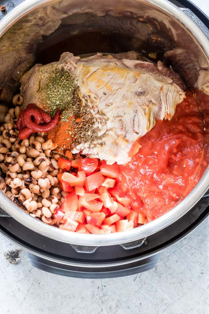 ingredients of campfire stew inside instant pot including tomatoes, pork joint, and beans
