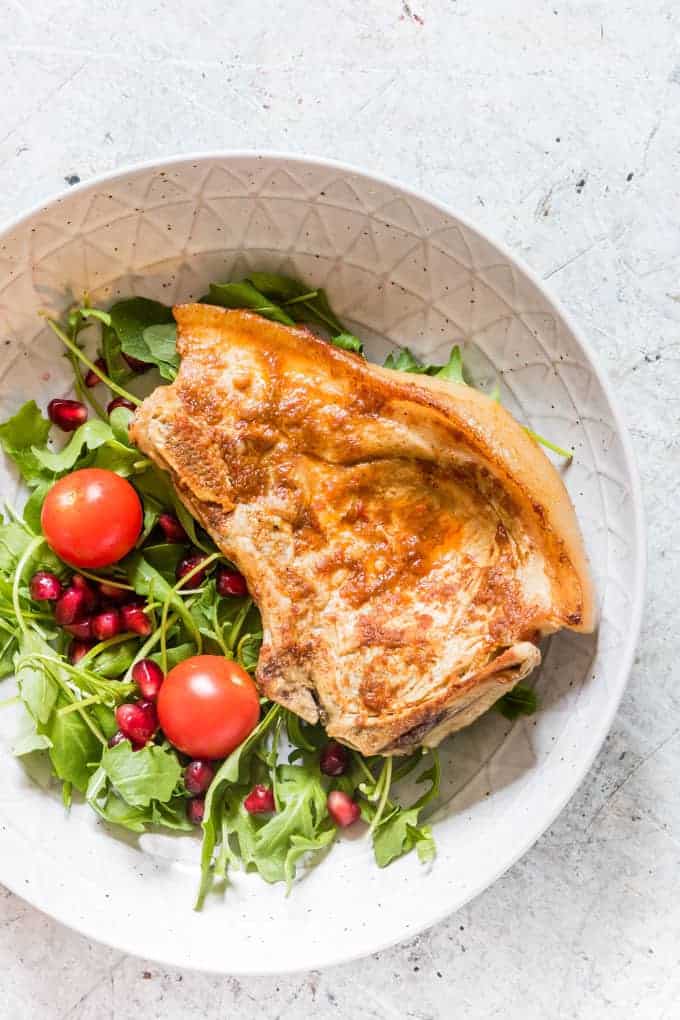 overhead view of instant pot pork chops in a white salad bowl next to salad greens