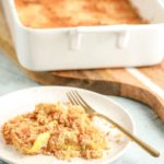 a serving of yellowe squash casserole on a white plate in front of the full casserole dish
