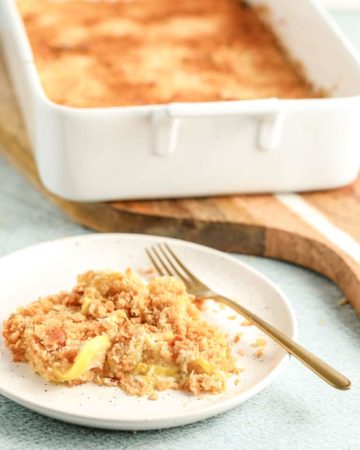 a serving of yellowe squash casserole on a white plate in front of the full casserole dish