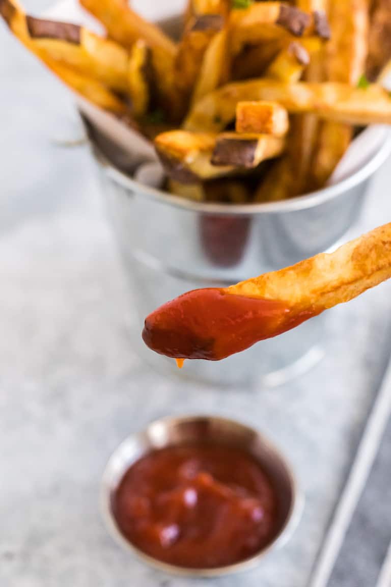 close up view of air fryer french fries with one fry being dipped in ketchup
