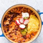 overhead view of chicken chilli with tortilla chips and sour cream on top