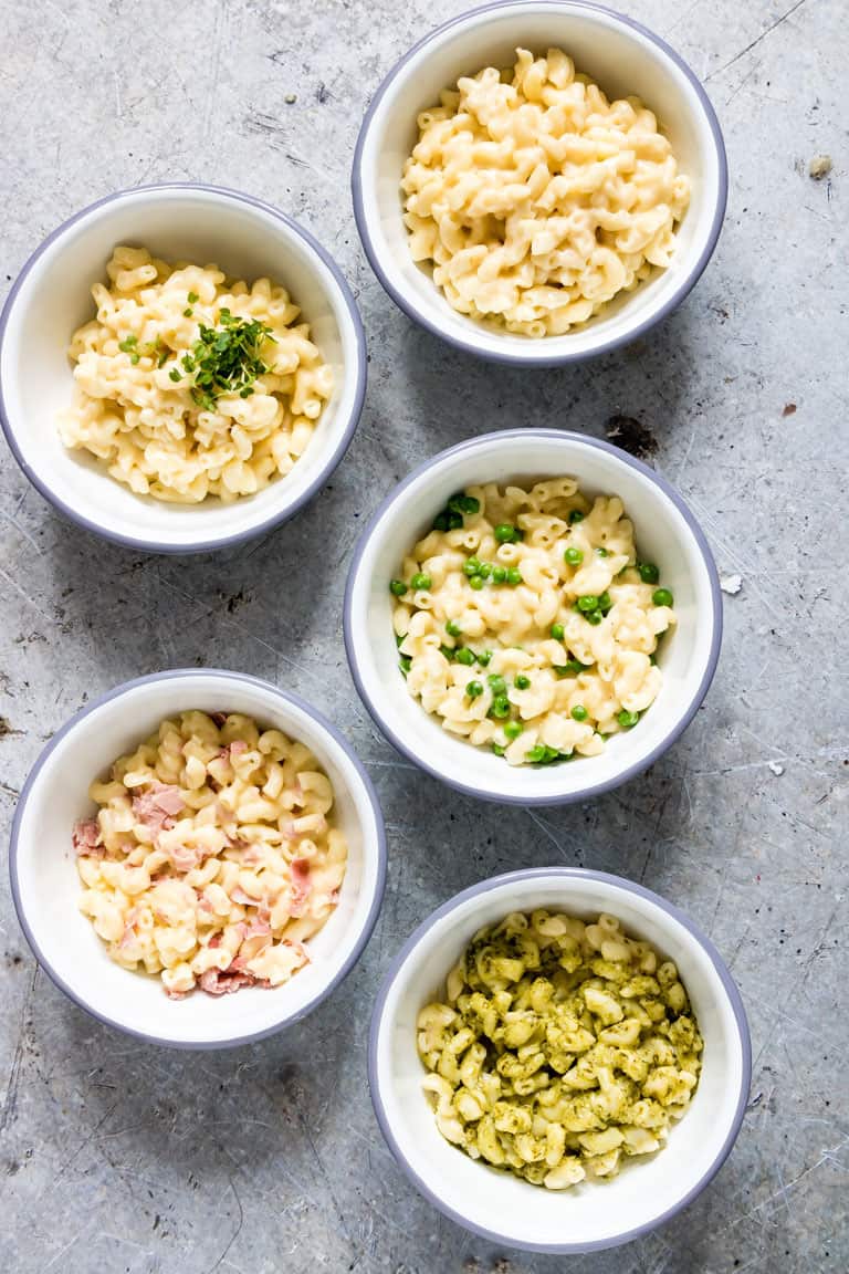 five white bowls with different varieties of instant pot mac and cheese on a countertop