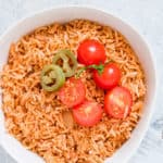 white bowl on a white countertop containing instant pot mexican rice with sliced tomatoes on top