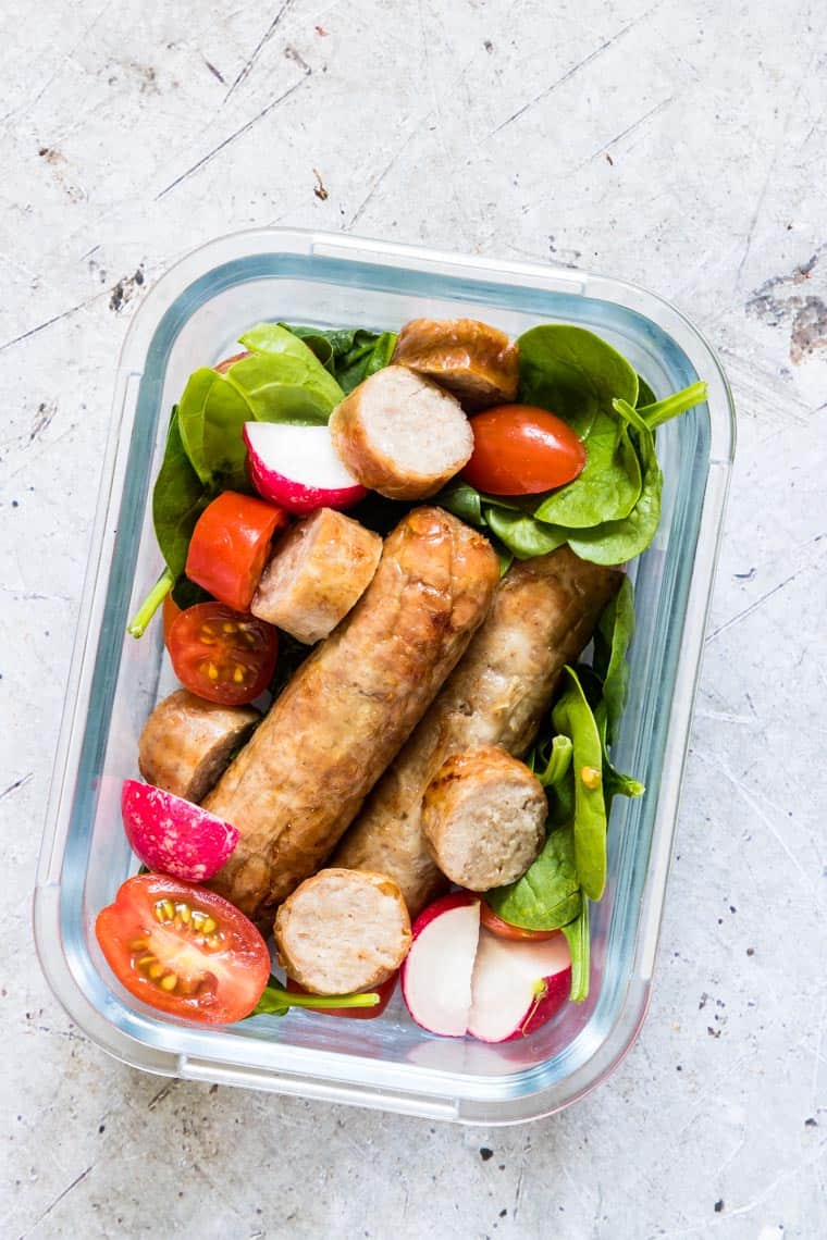 air fryer sausages inside a glass meal prep container with a green salad