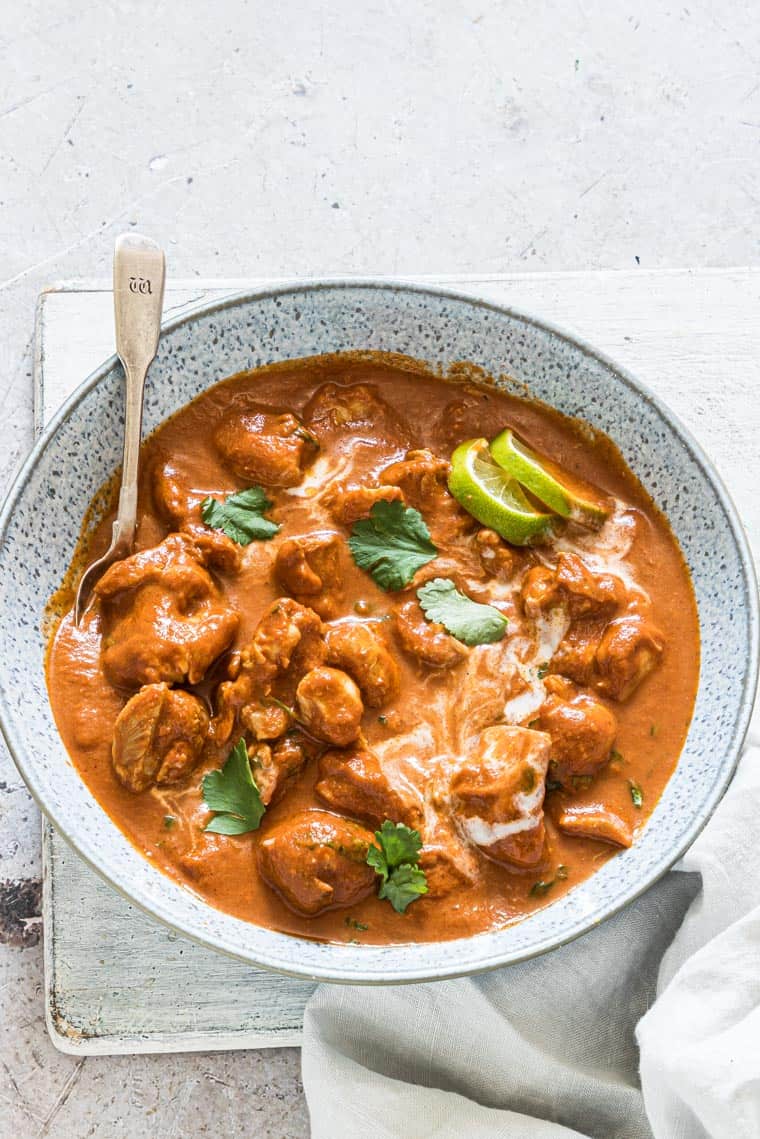a bowl filled with the instant pot butter chicken and a silver spoon inside