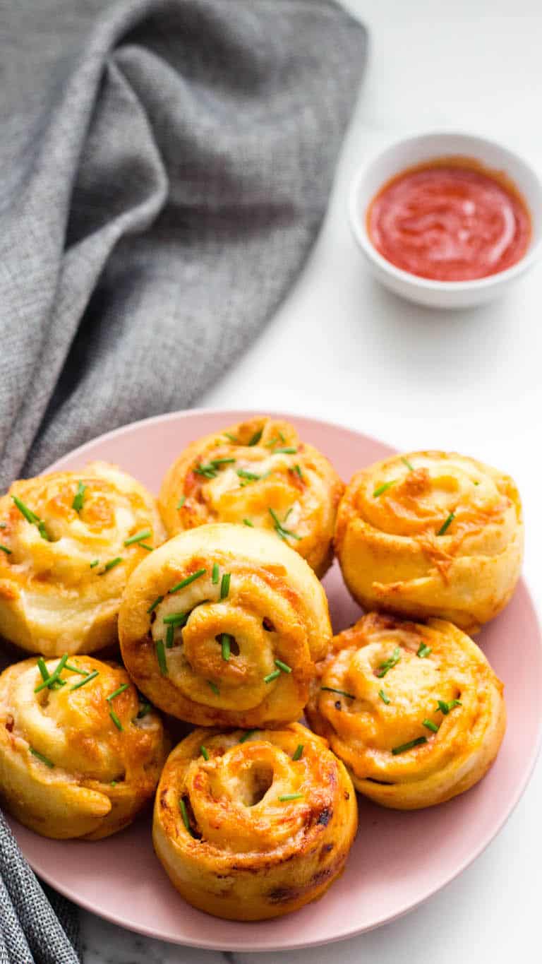 a plate of cooked air fryer pizza rolls ready with a small bowl of marinara sauce