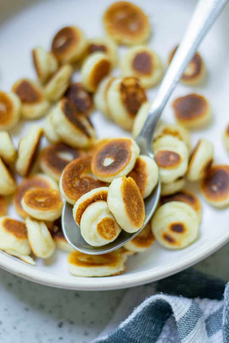 a close up view of a spoonful of mini pancakes being removed from a bowl