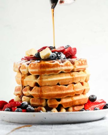 a stack of buttermilk waffles topped with fresh berries, butter and maple syrup