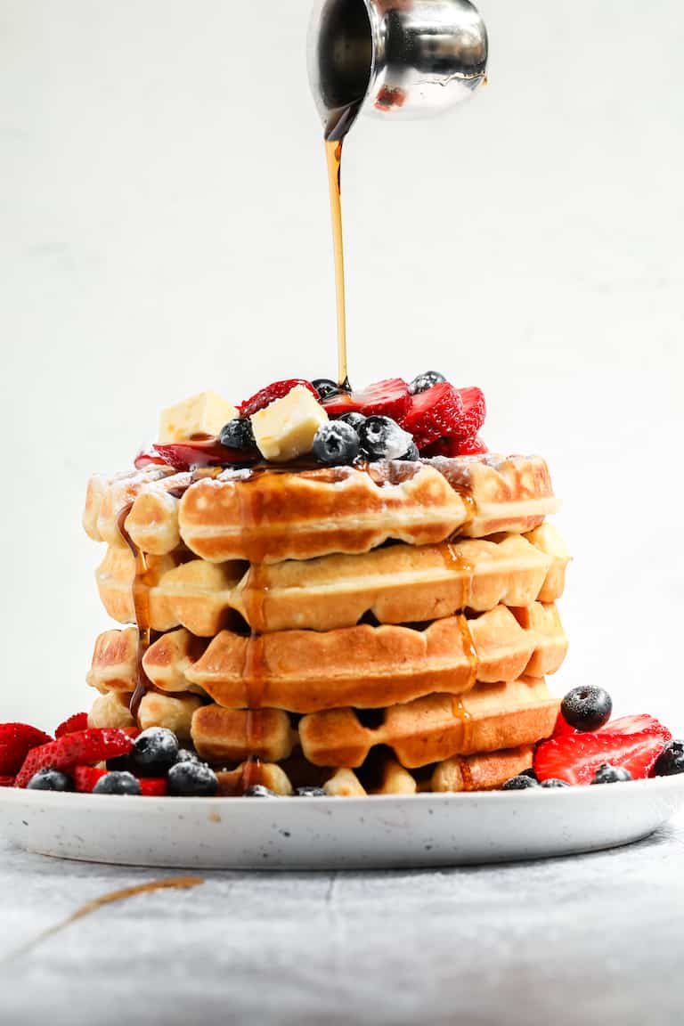 a stack of buttermilk waffles topped with fresh berries, butter and maple syrup