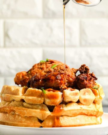 profile view of chicken and waffles with maple syrup being poured on top