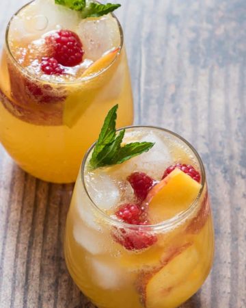 two completed peach bourbon smash cocktails garnished with fresh fruit and mint leaves