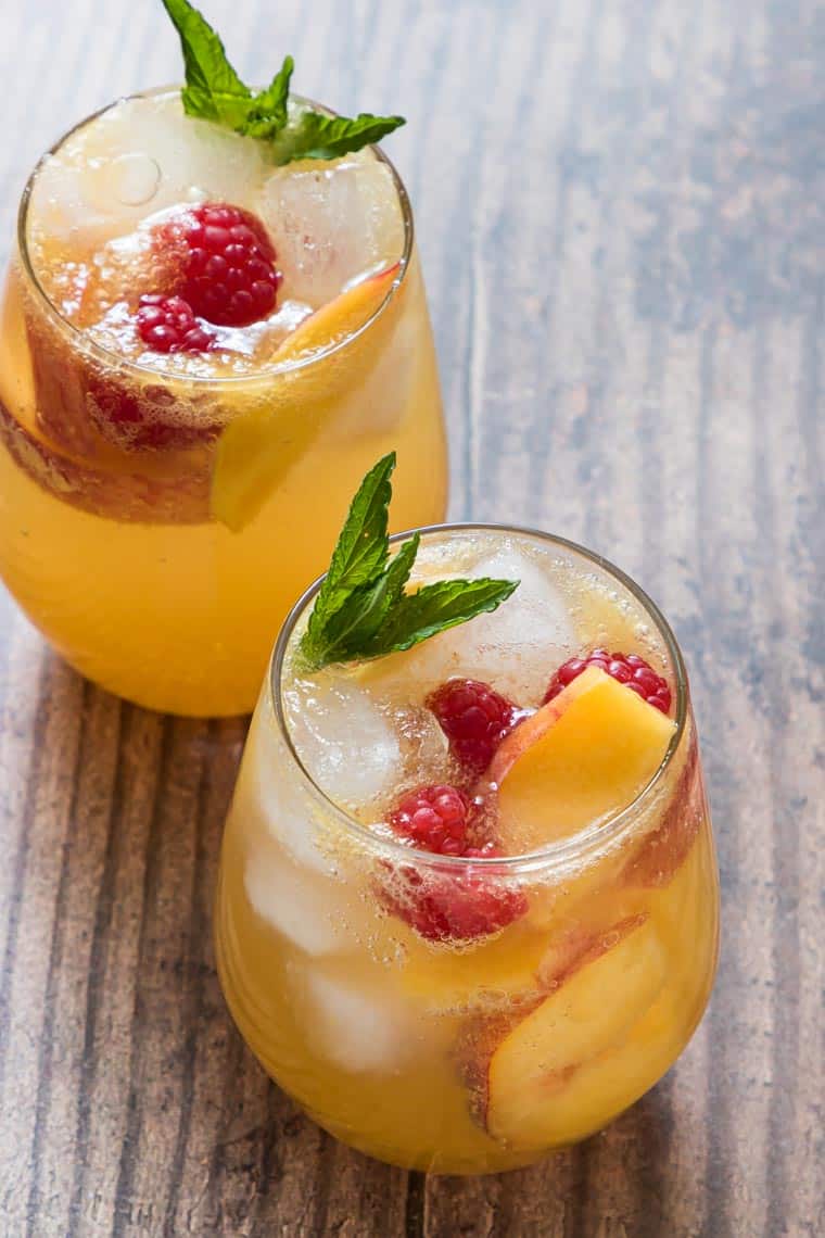 two completed peach bourbon smash cocktails garnished with fresh fruit and mint leaves