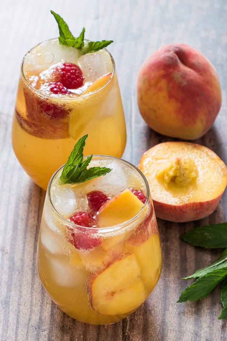 two peach bourbon smash cocktails next to a fresh peach