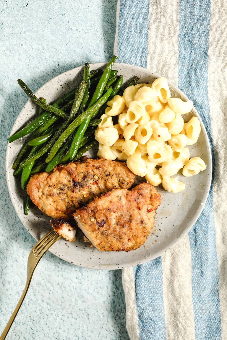 top down view of a plate filled with two fried pork chops, green beans and mac and cheese