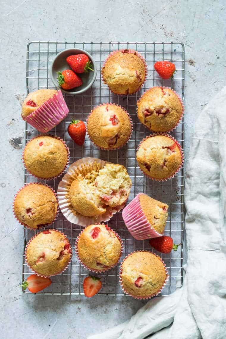 freshly baked orange strawberry muffins on a cooling rack with extra strawberries