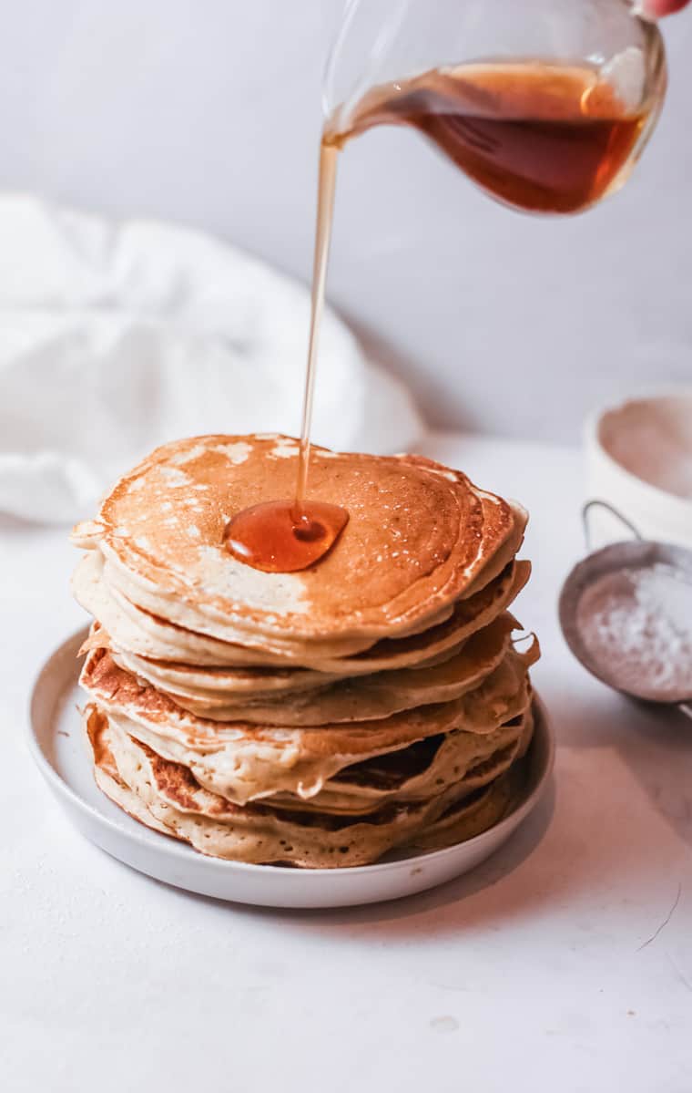 a stack of buttermilk pancakes with syrup being poured on top